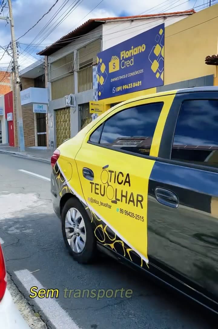 Carro amarelo e preto adesivado com o logo da Ótica Teu Olhar, parado numa rua de Floriano.